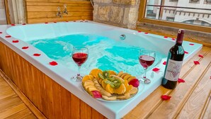 A bathtub with rose petals, two glasses of red wine, and a bottle of wine on a wooden floor. - Tantan Cappadocia House (Nevsehir)