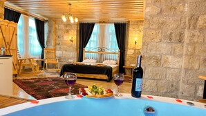 A bedroom with a large bed, a wooden ceiling, stone walls, and a hot tub with fruits and wine glasses. - Tantan Cappadocia House (Nevsehir)