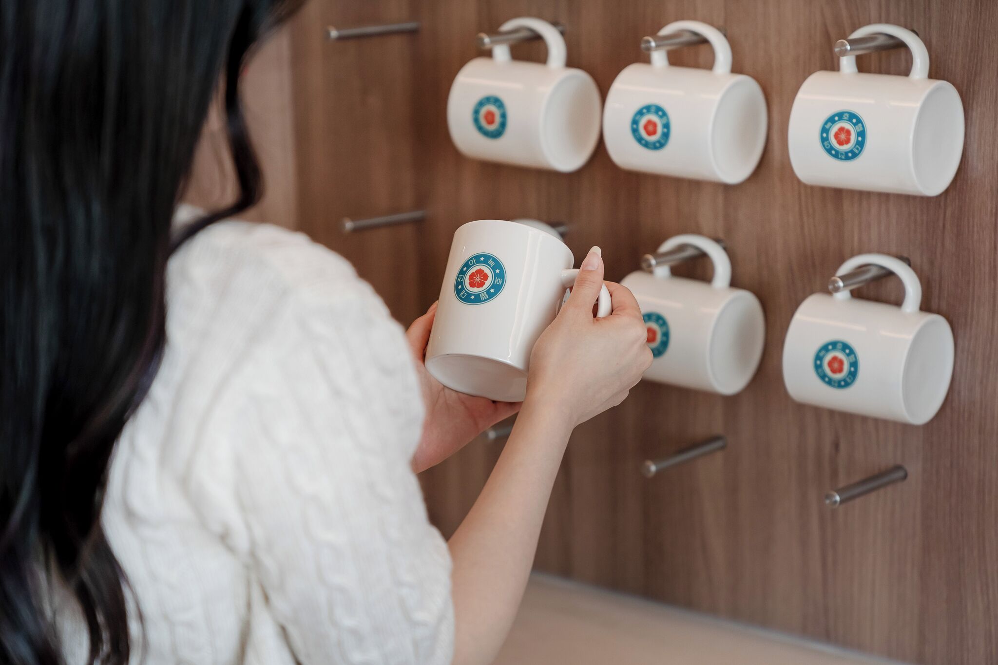 Una persona sosteniendo una taza con asa, y varias tazas similares colgadas en el fondo.