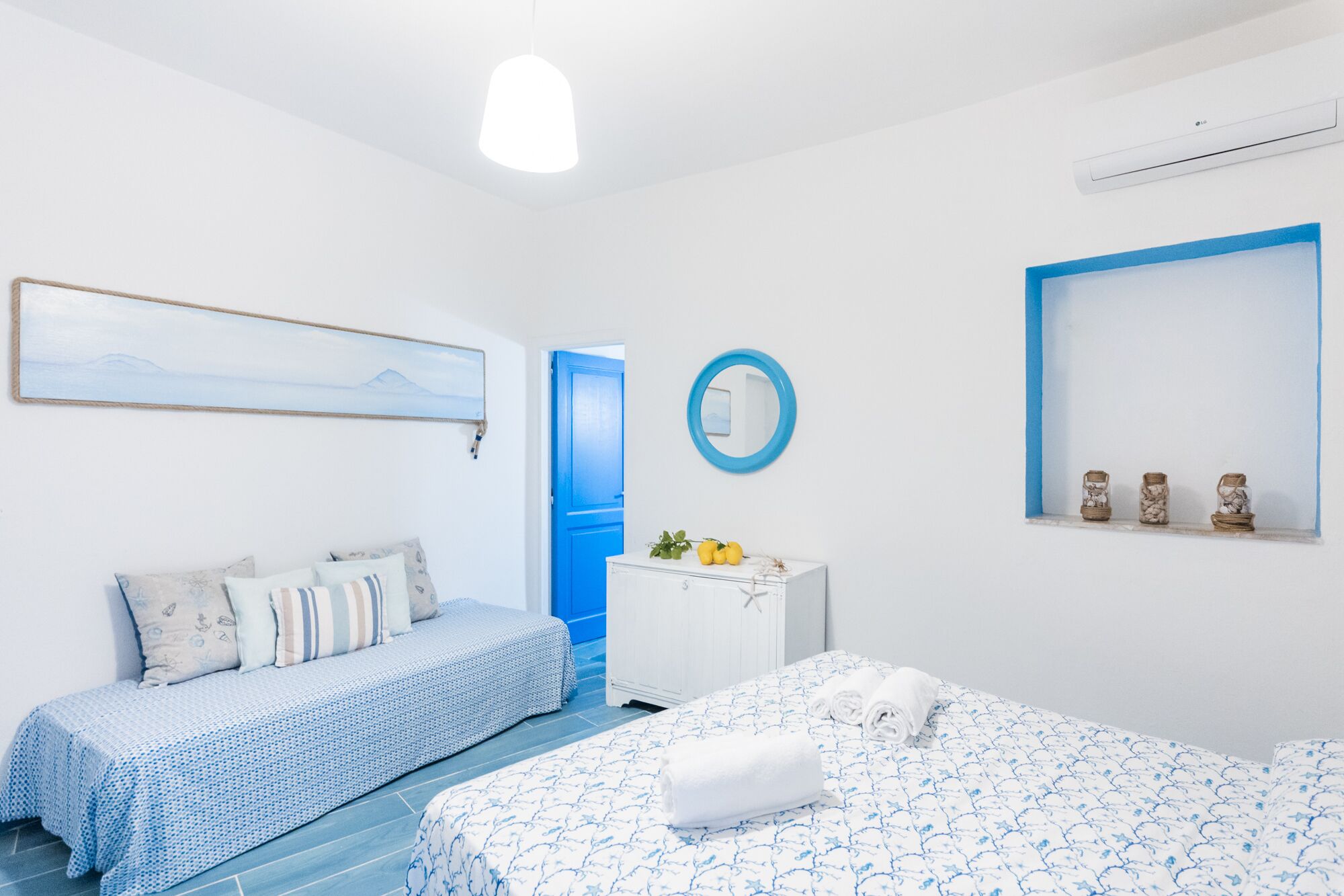 Une pièce comprenant un lit, un canapé, une petite table agrémentée d’objets décoratifs, un miroir et un tableau au mur.