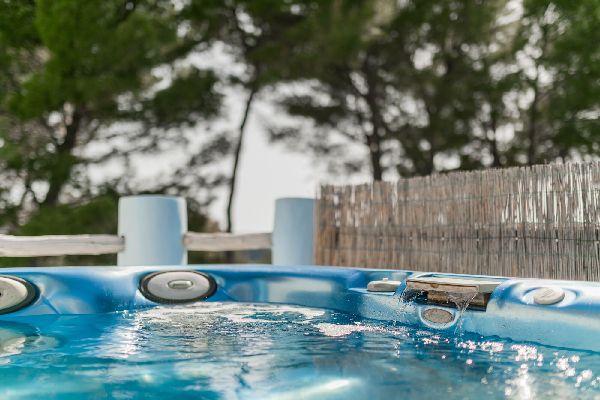 Un jacuzzi con chorros de agua, rodeado por una valla de madera y árboles al fondo.