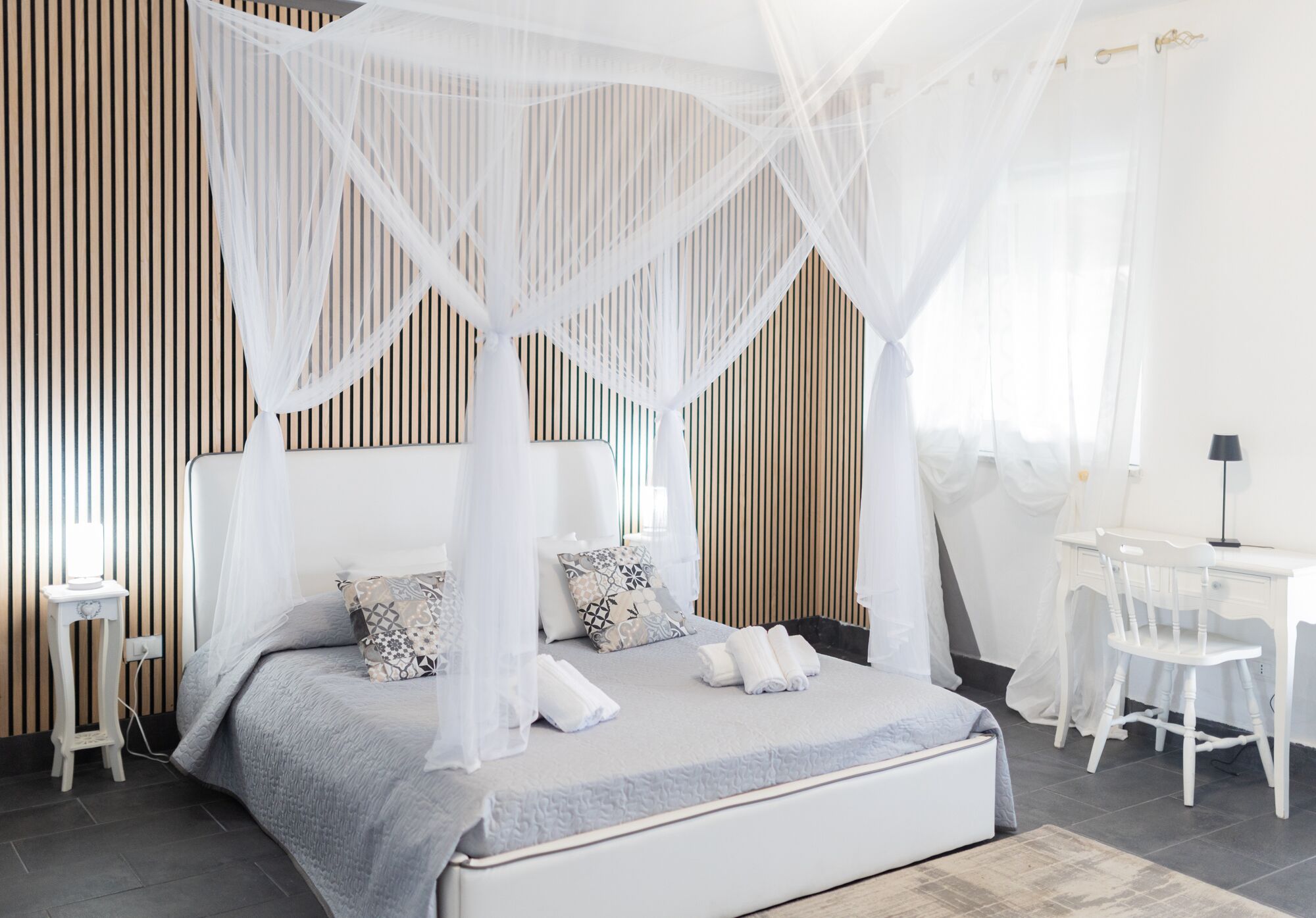A modern bedroom with a canopy bed, bedside tables, a desk, and a chair.