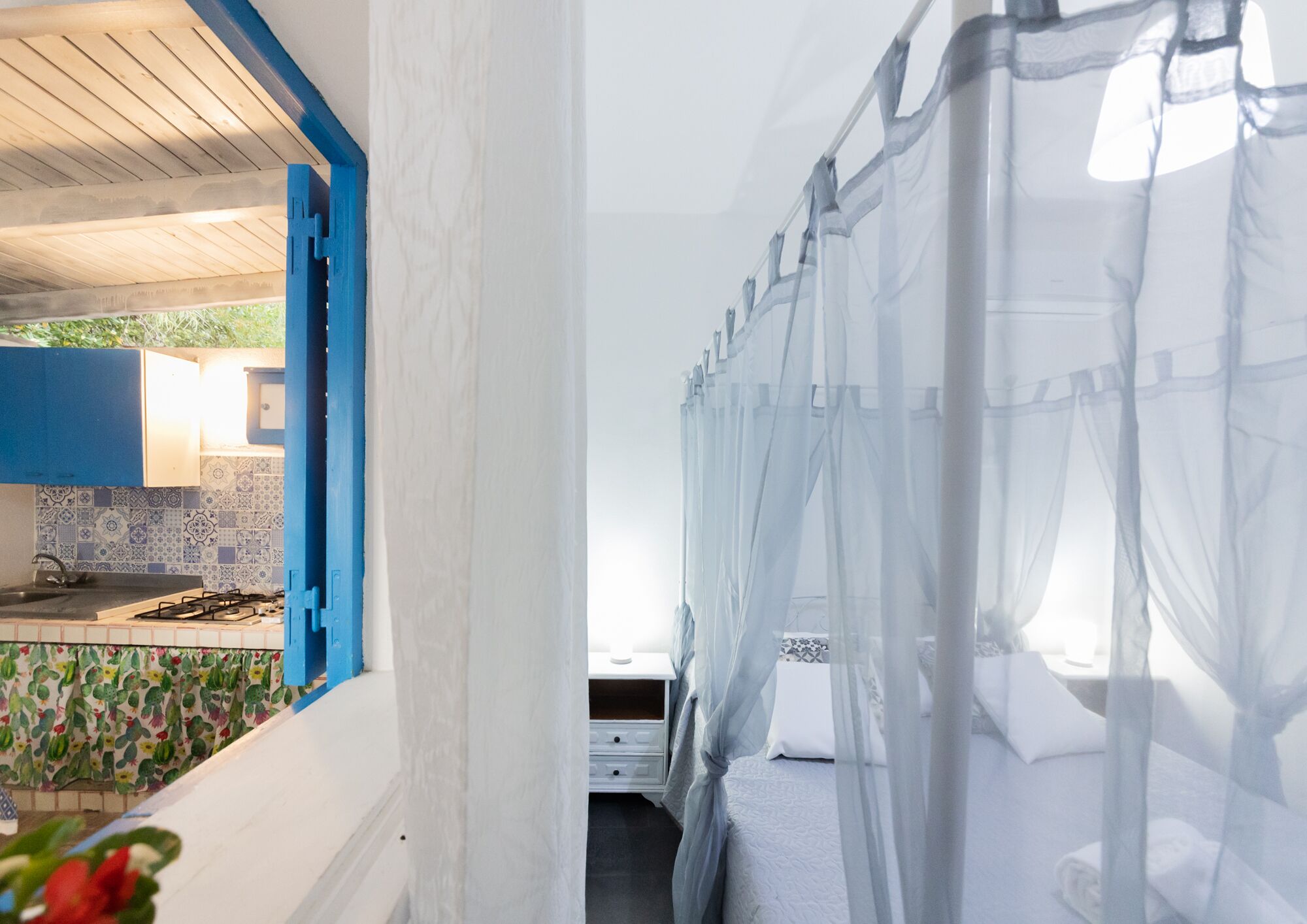 A bedroom with a canopy bed, a kitchen with blue cabinets, and a tiled backsplash.