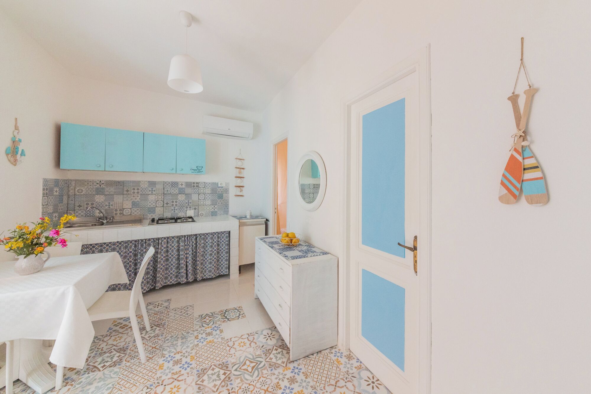 A compact kitchen with a tiled backsplash, a white sink, and a blue cabinet.