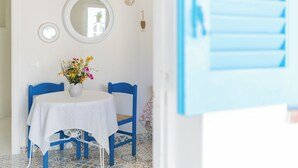 A room with a round table covered with a white tablecloth, blue chairs, a vase with flowers, a round mirror, and a blue shutter door. - Holiday Eolie Village (Lipari)