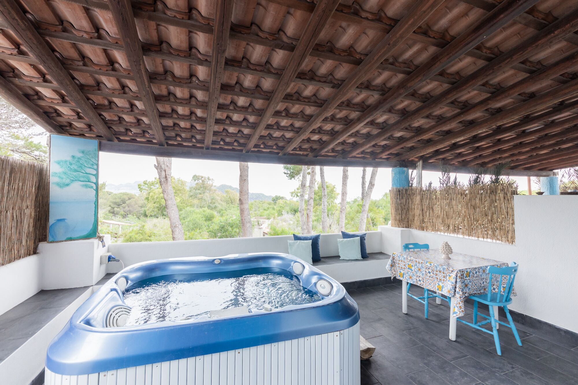 A covered outdoor area with a hot tub, seating, and a table.