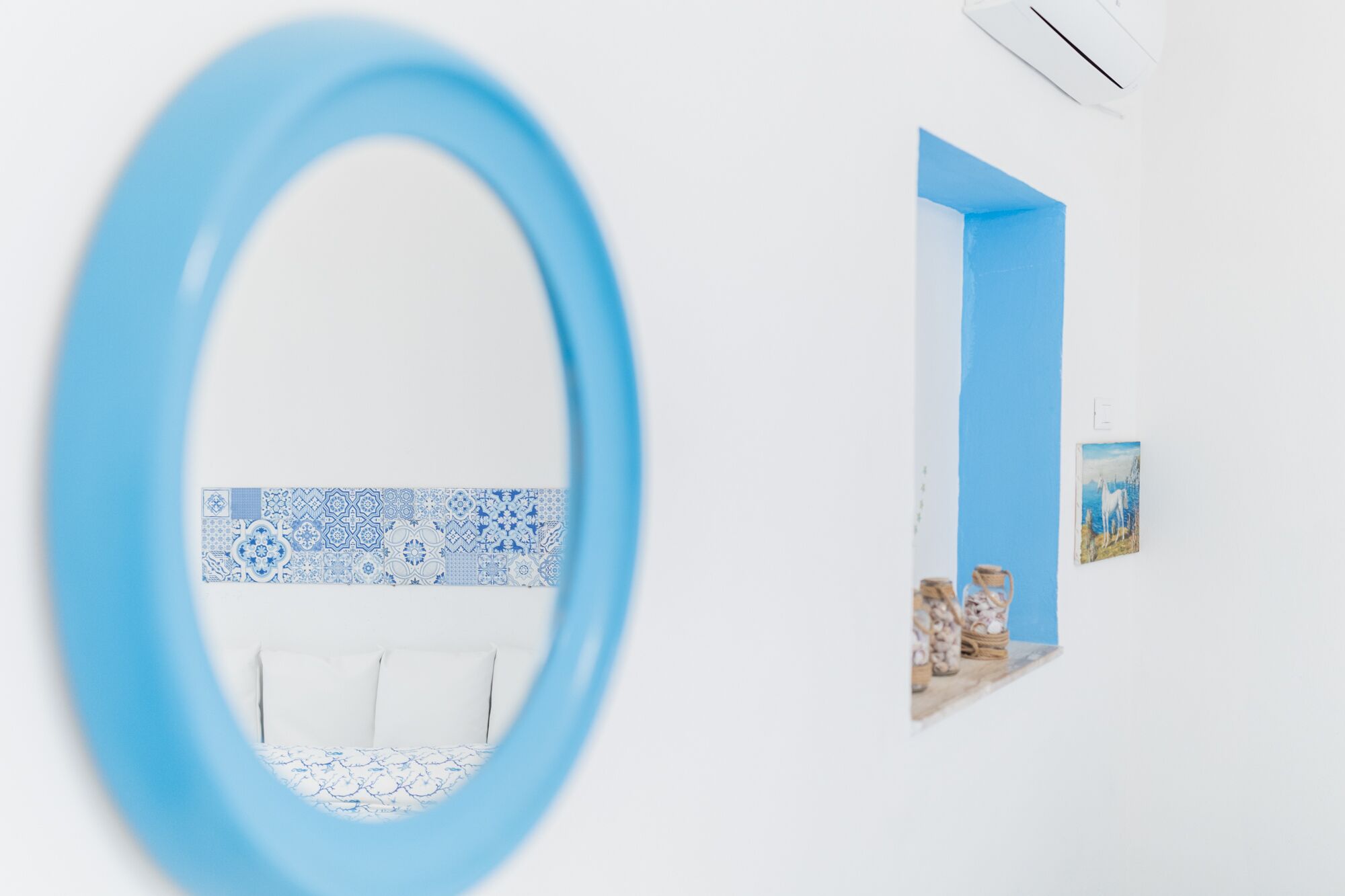 A room with a white wall, a blue decorative border, a white sofa, and a small shelf with decorative items.