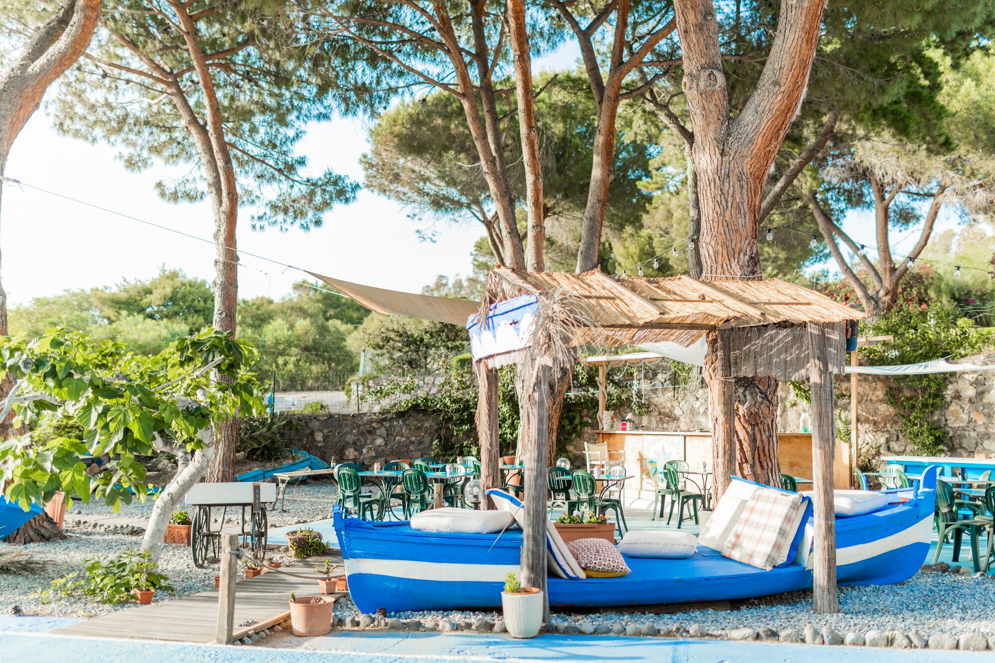 A blue boat with a canopy, surrounded by green chairs and potted plants.
