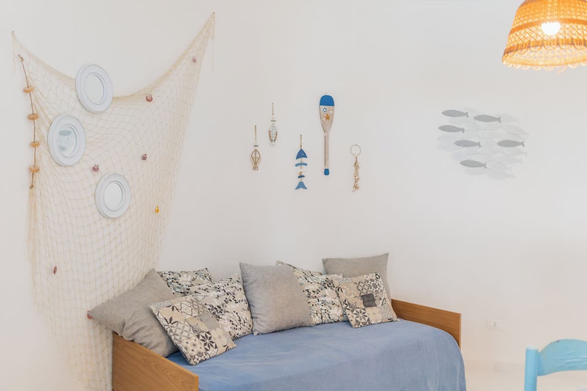A bedroom with a bed, pillows, a hanging net, and wall decorations including a lamp, keychain, and fish silhouette.