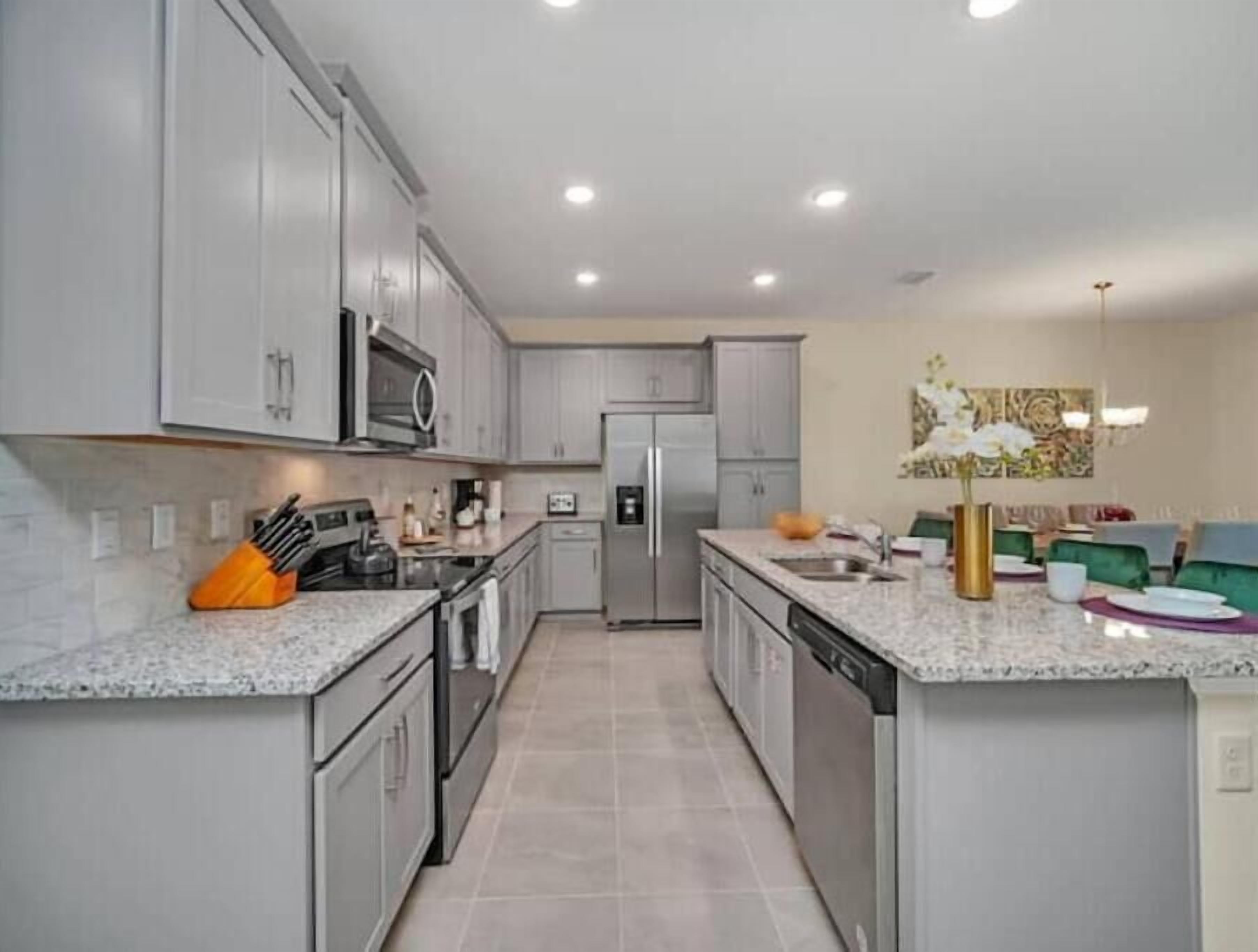 A modern kitchen with grey cabinets, stainless steel appliances, and a marble countertop.