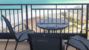 Varanda com mesa redonda e quatro cadeiras, vista para uma praia e oceano.