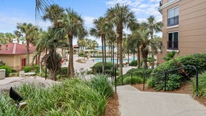 Uma área de resort com palmeiras, piscina e um edifício com varandas.