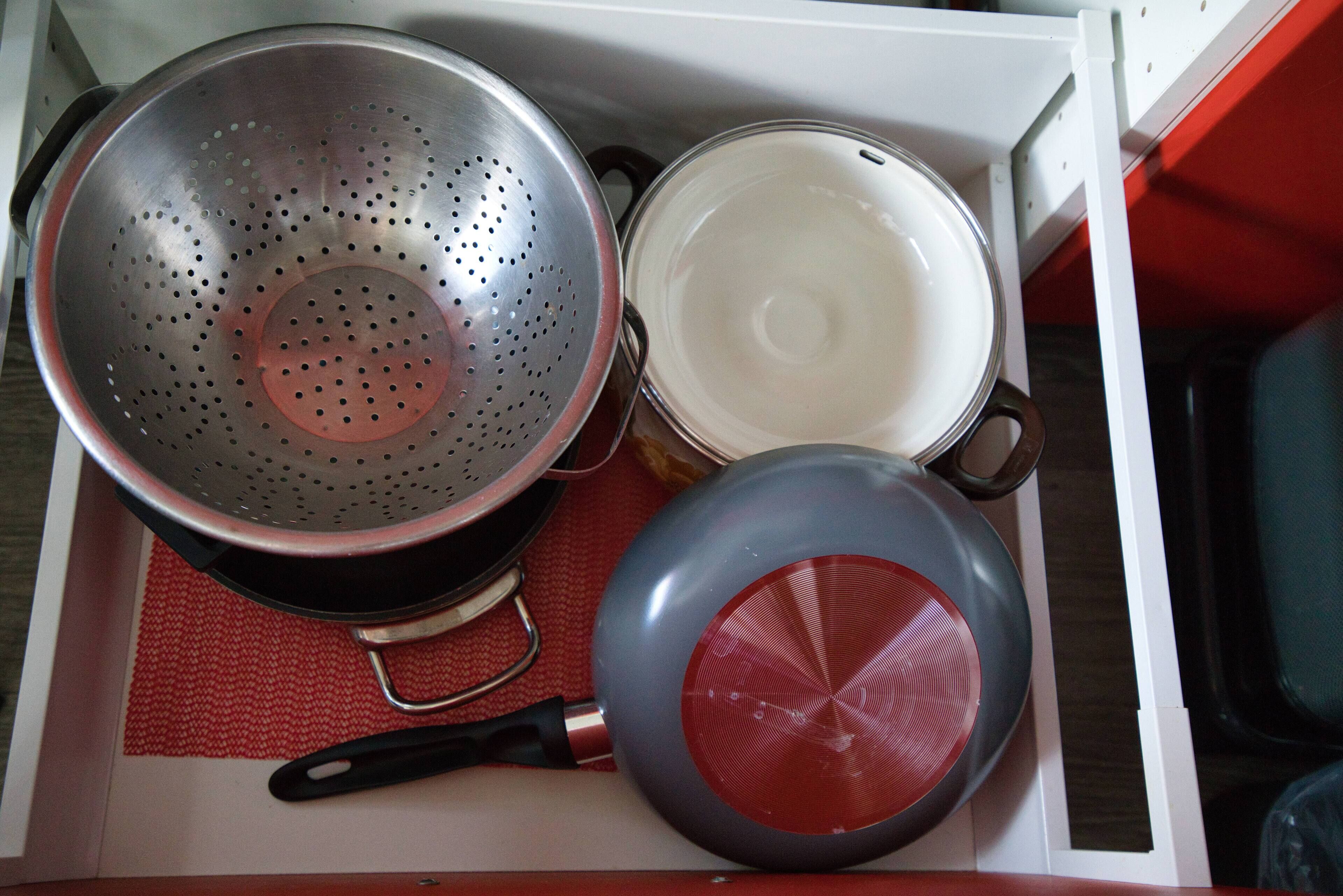 Un cajón de cocina con un colador, una sartén y una olla.