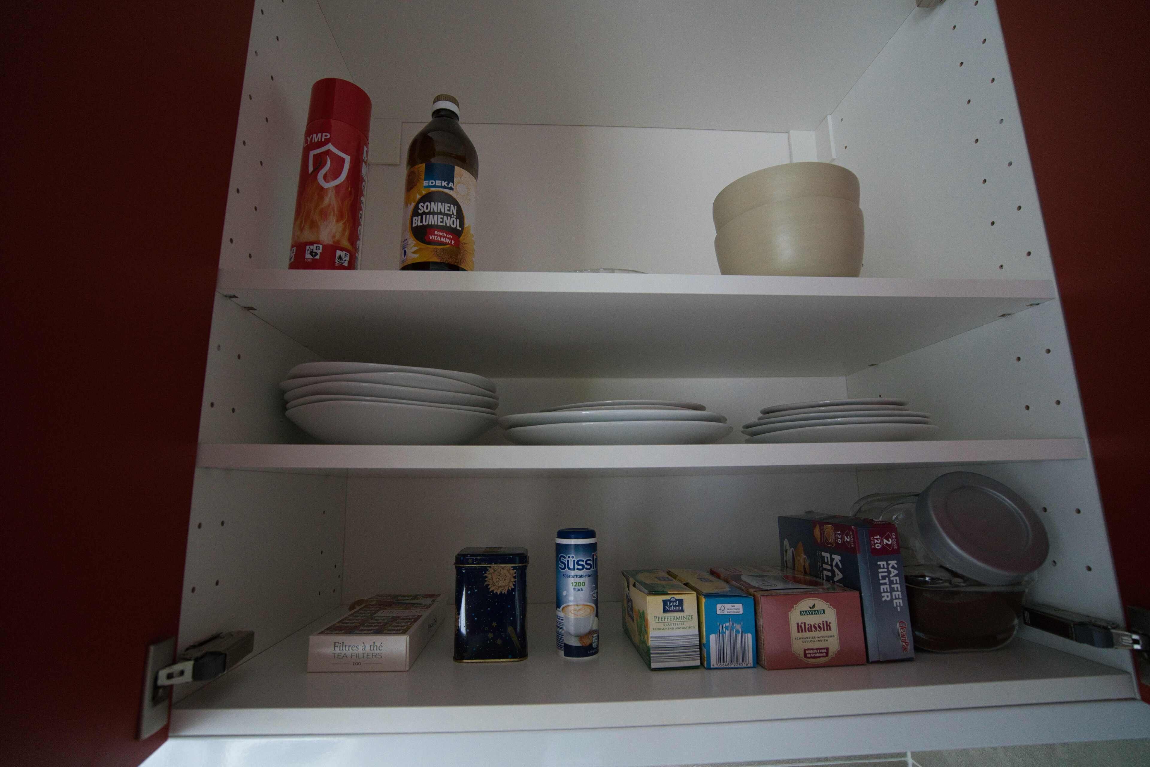 Una estantería de cocina con diversos objetos, incluyendo una lata de café, una caja de filtros de café y un envase de crema para café.