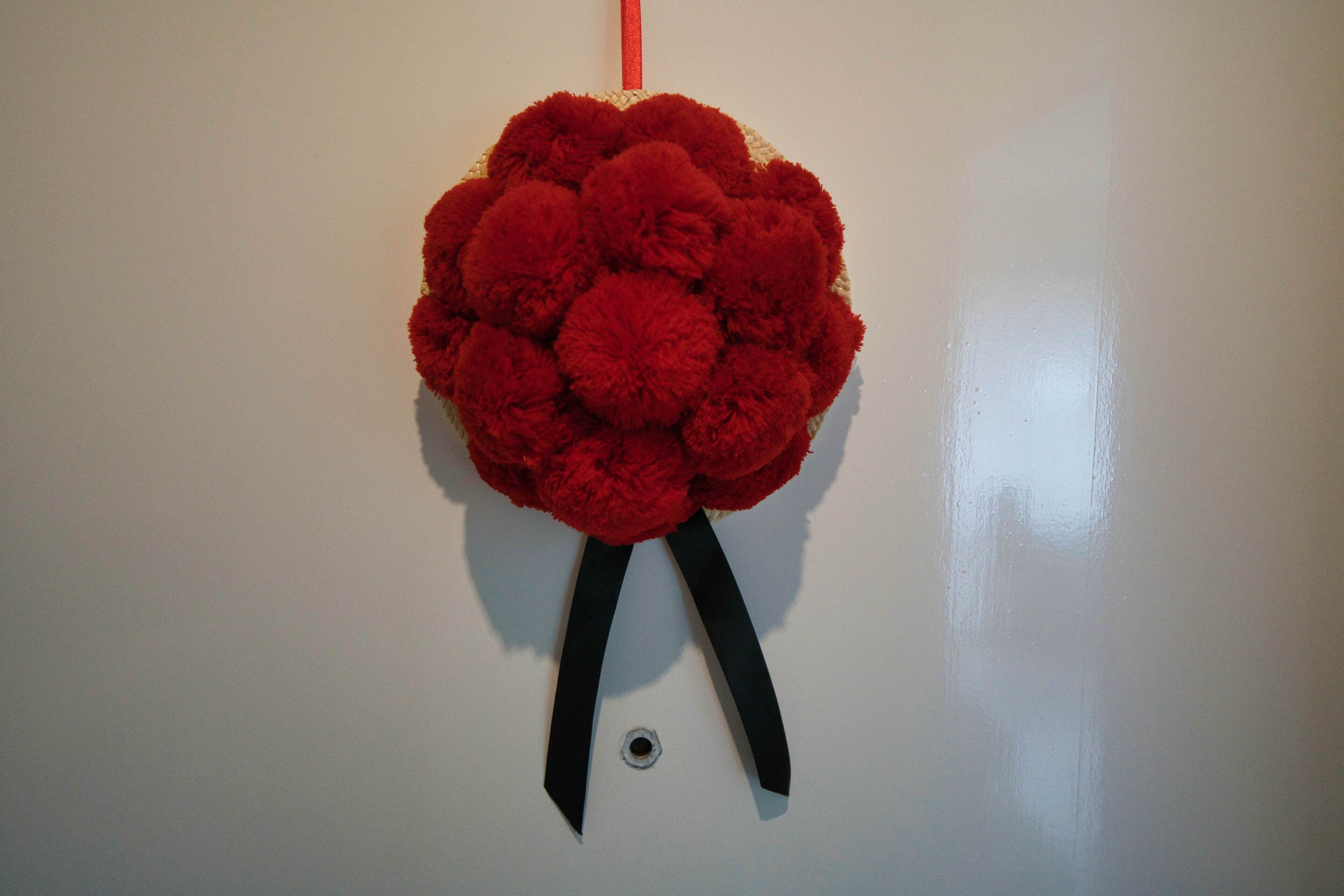 A red pom-pom decoration with black ribbons on a white wall.