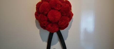A red pom-pom decoration with black ribbons on a white wall.