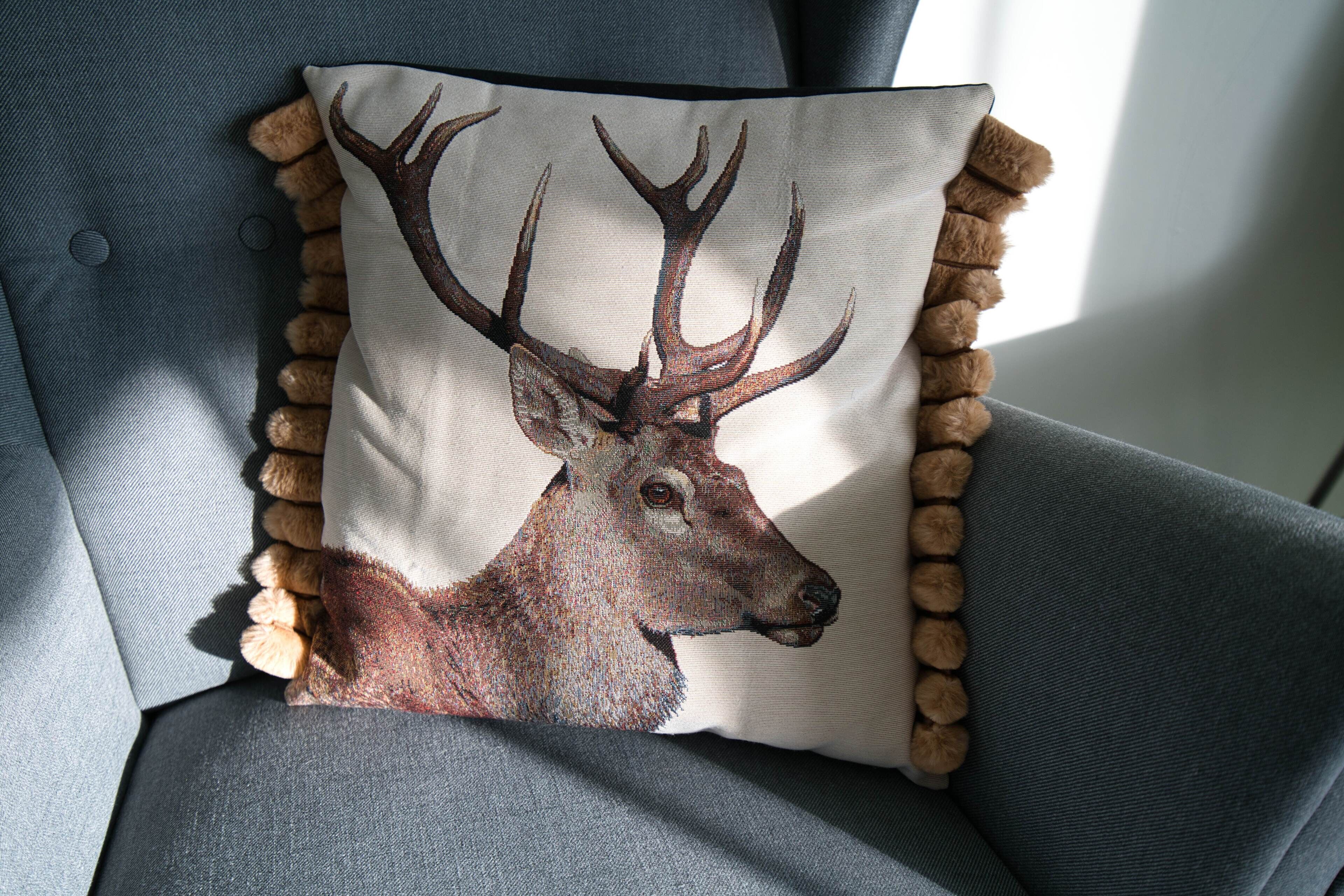 A pillow with a deer illustration on a grey upholstered chair.