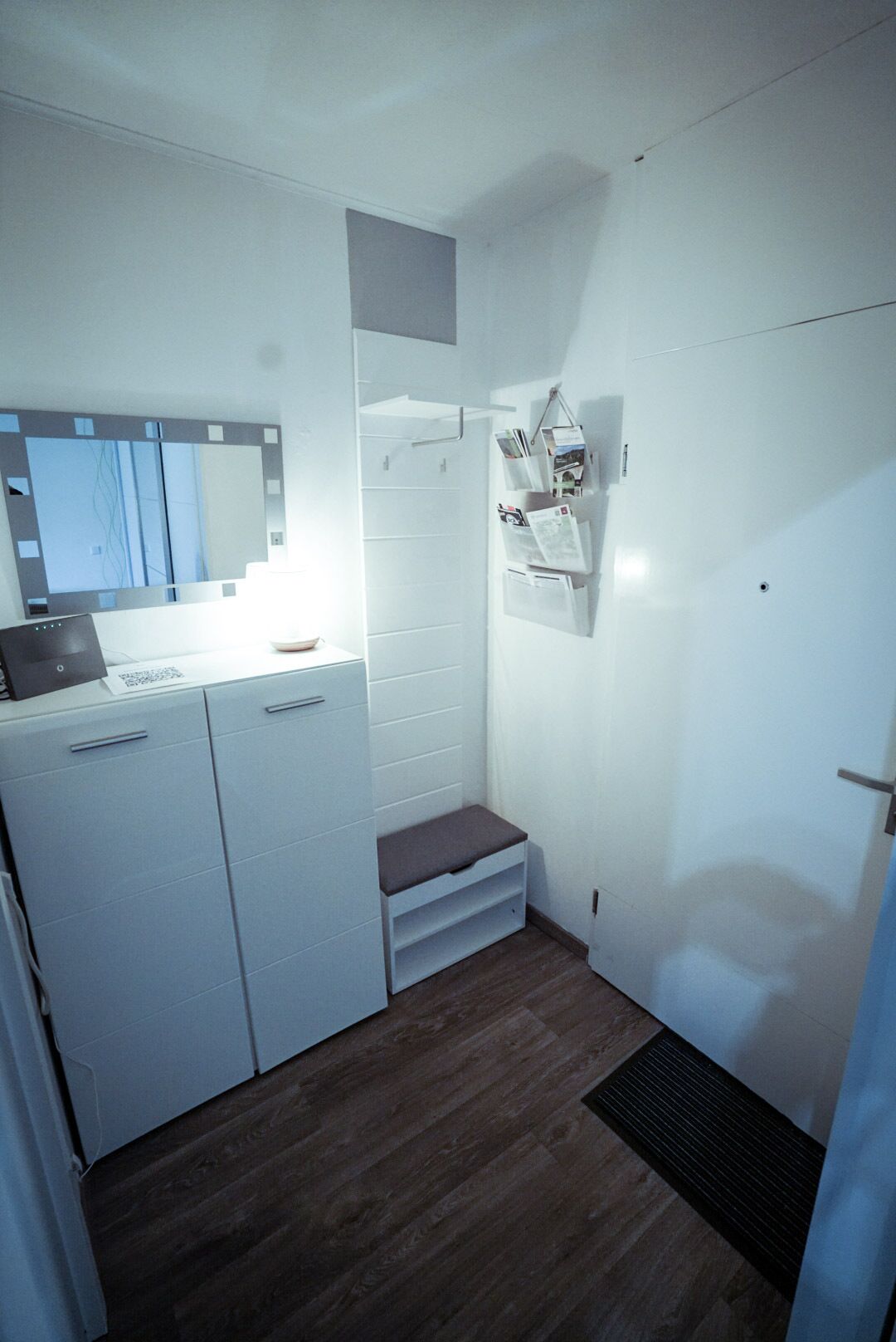Eine kompakte Küche mit integriertem Kühlschrank, Mikrowelle und Spüle. Vor einer Tür befindet sich eine kleine Stufe, und eine Wandhalterung trägt diverse Gegenstände.