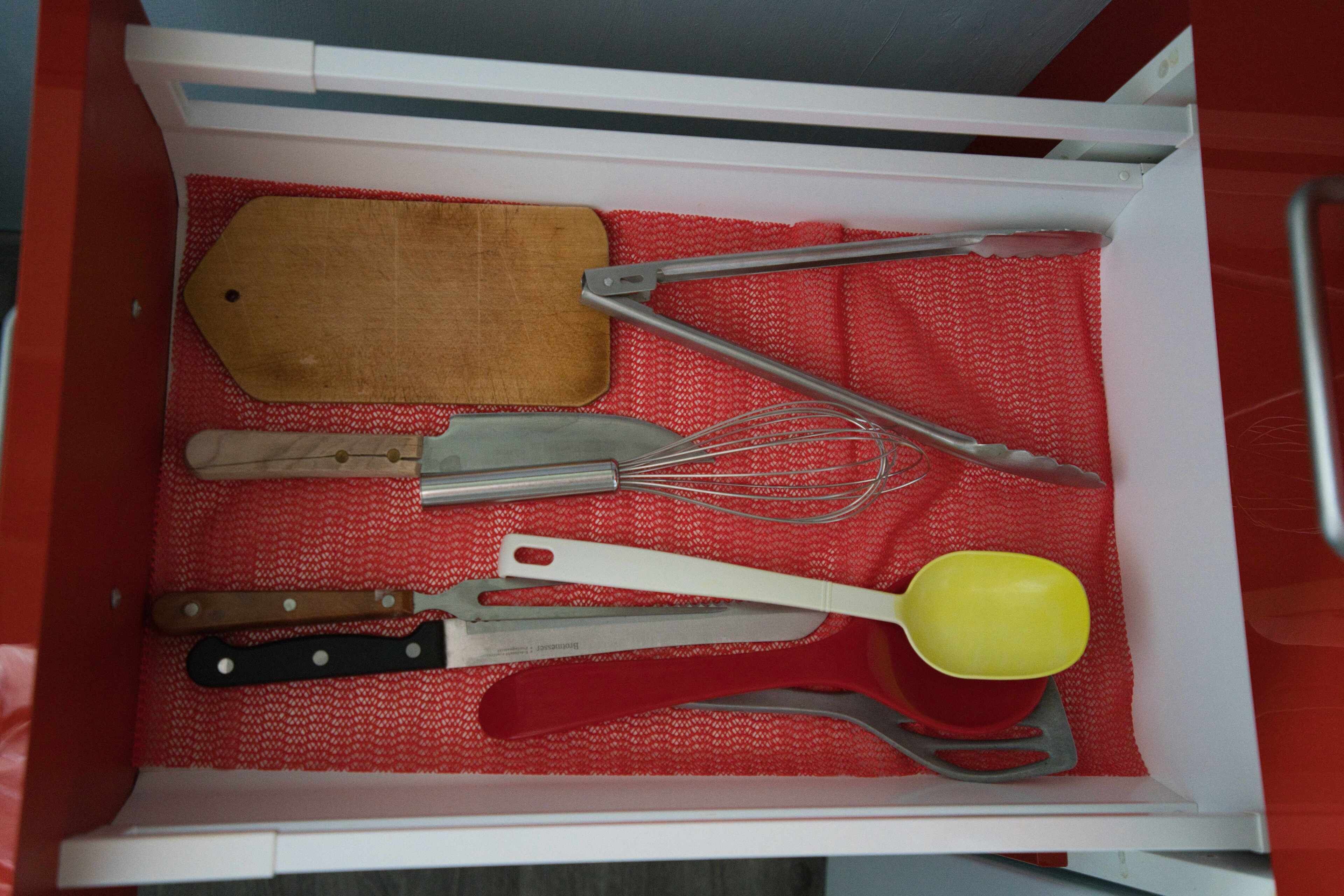 A drawer with a red cloth lining containing various kitchen utensils.