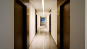 Un couloir d’hôtel moderne, avec un sol ciré, des portes en bois et un éclairage supérieur lumineux.
