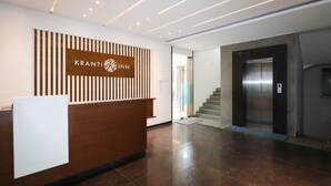 Un hall d'accueil moderne avec un comptoir en bois, une enseigne indiquant « KRANTI INN » et un ascenseur.