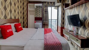 A hotel room with a bed, a TV, a desk, and a wardrobe. - OYO Life 92910 Apartemen Tamansari Panoramic By Tira (Bandung)