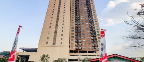 A tall, beige building with multiple balconies and a flag on the left.