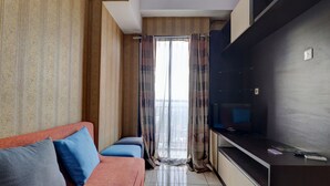 A hotel room with a sofa, a TV, and a window with curtains. - OYO Life 92910 Apartemen Tamansari Panoramic By Tira (Bandung)
