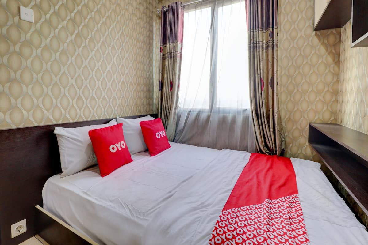 A hotel room with a bed, two pillows with 'OYO' branding, a window with sheer curtains, and a patterned wall.