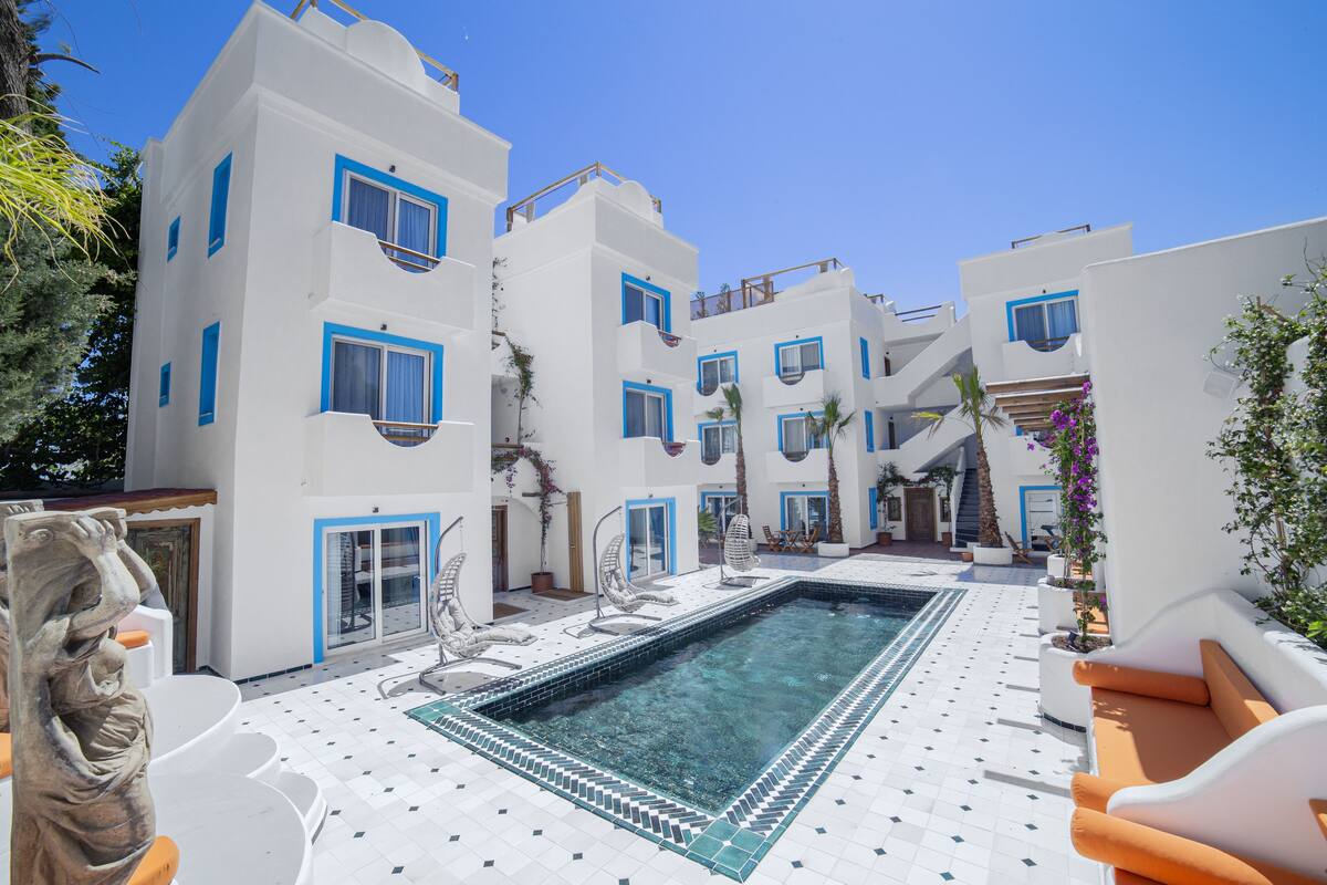 A pool area with white buildings, blue accents, and a clear blue sky.