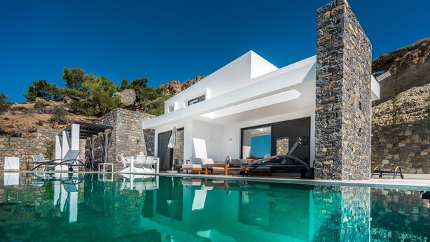 Una villa moderna con piscina, muros de piedra y mobiliario exterior.