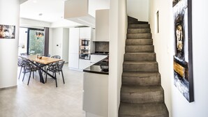 Una cocina moderna con electrodomésticos integrados, un comedor con mesa y sillas de madera, y una escalera que sube a otro nivel.