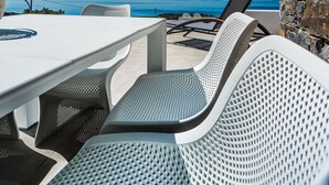 Una terraza con mesa y sillas blancas, con vista a un cielo azul despejado y al mar.