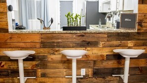 Une cuisine avec un lambris en bois, un grand miroir et trois tabourets de bar blancs.