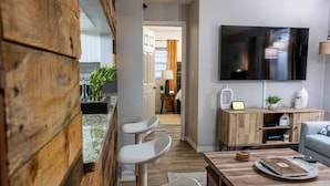 Un salon moderne avec un mur d’accent en bois, un téléviseur à écran plat, un meuble en bois et un coin salon avec des chaises blanches.