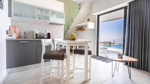 Una cocina moderna con armarios blancos, un comedor con mesa blanca y sillas marrones, y vista a una piscina a través de amplios ventanales.