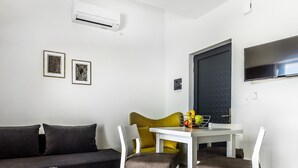 Una sala de estar moderna con un sofá, una mesa de comedor con sillas, un televisor y un equipo de aire acondicionado.