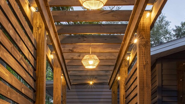 Una pérgola de madera con un sendero de ladrillo que lleva a un edificio oscuro.