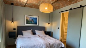 A bedroom with a large bed, two bedside tables, a hanging light fixture, a framed picture on the wall, and a sliding door. - Villa Bricco 46 - beautiful villa to rent in Piemonte Italy. (Nizza Monferrato)
