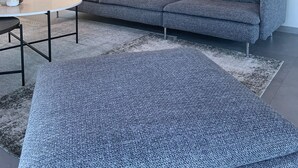 A modern living room with a grey sofa, a round coffee table, and a patterned rug. There are two framed pictures on the wall, a lamp, and a chair in the background. - Villa Bricco 46 - beautiful villa to rent in Piemonte Italy. (Nizza Monferrato)