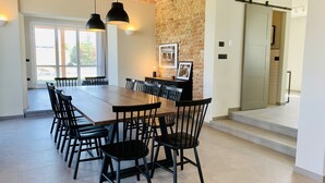 A spacious dining area with a long table and black chairs, a brick wall, and a sliding door leading to another room. - Villa Bricco 46 - beautiful villa to rent in Piemonte Italy. (Nizza Monferrato)