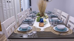 Une table à manger dressée avec de l’argenterie, des verres transparents et de l’assiette bleue et blanche, entourée de chaises blanches.