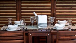 A wooden dining table set with white plates, bowls, and glasses, and a bottle of champagne.