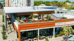 A modern building with a rooftop patio area, a sign reading "TAMPA ARMATURE," and a view of surrounding buildings and greenery.