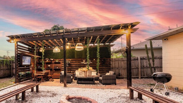 A covered outdoor seating area with a wooden pergola, wicker furniture, and a barbecue grill.
