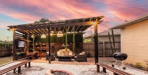 Ein überdachter Außenbereich mit Holz-Pergola, Korbmöbeln und einem Grill.