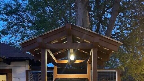 A wooden structure with a glass door, possibly a shed or a small pavilion, with a light fixture above the door. - LA CASITA ON EAST 7TH STREET (Austin)