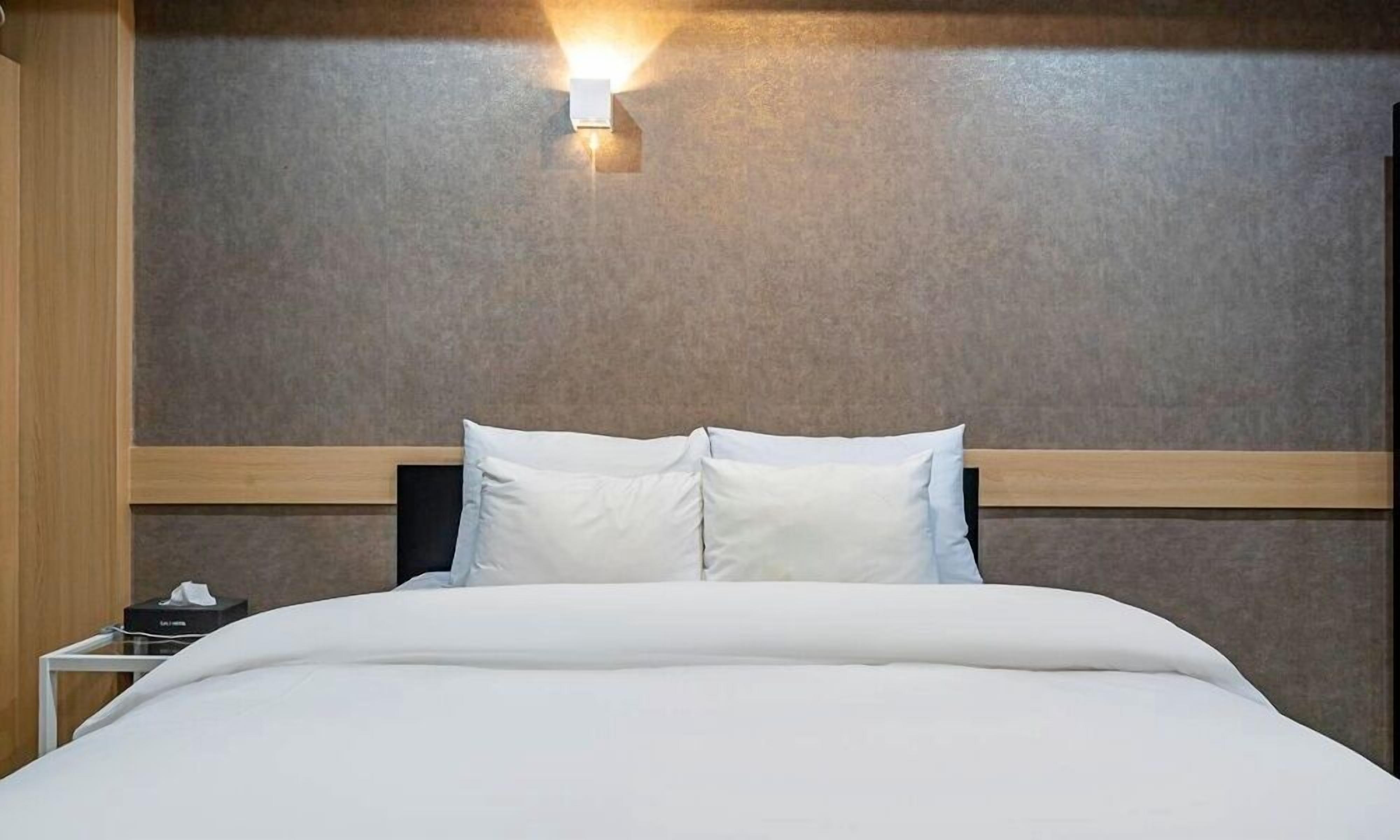A hotel room with a wooden headboard, a white bedspread, and a wall-mounted light fixture.