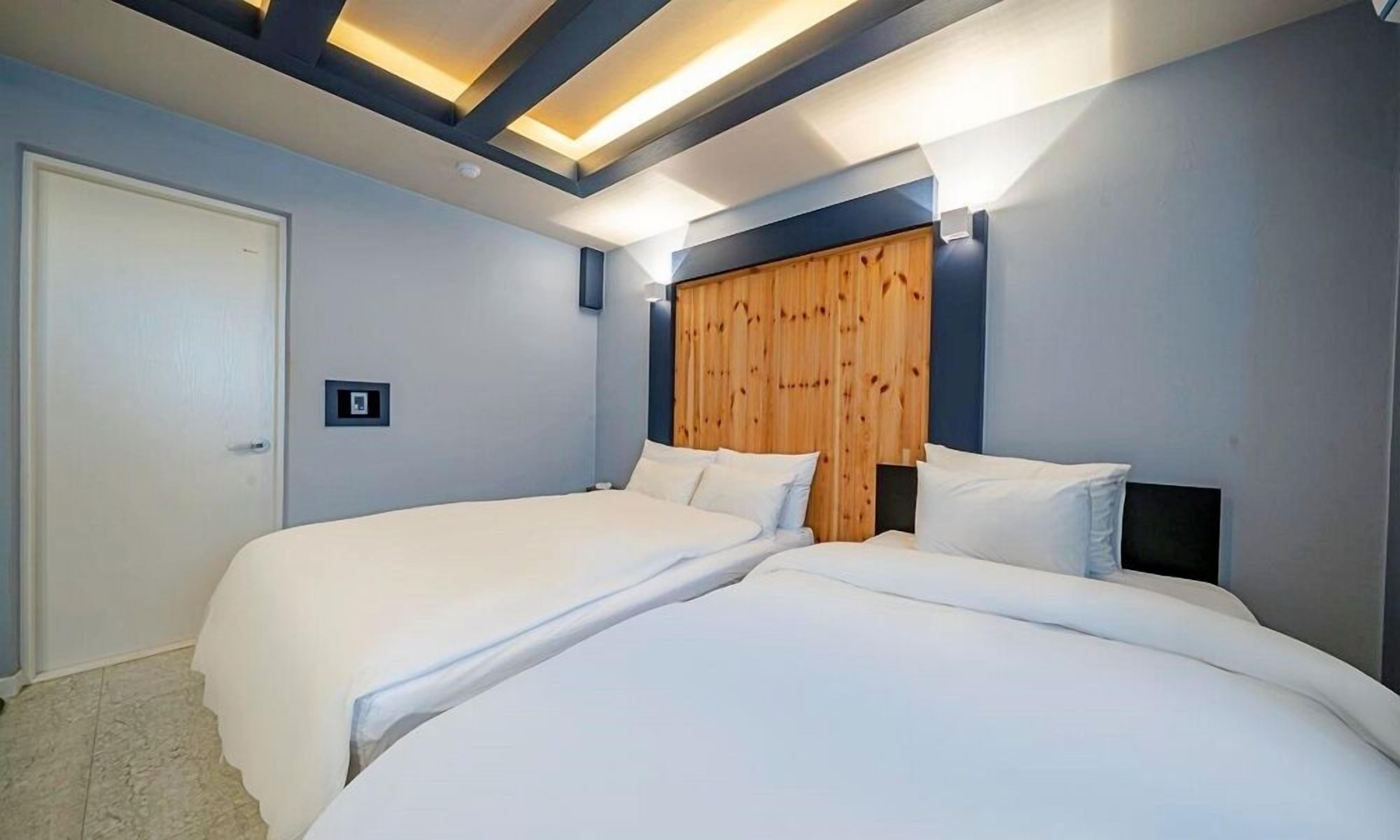 A bedroom with two beds, a wooden headboard, and recessed ceiling lighting.