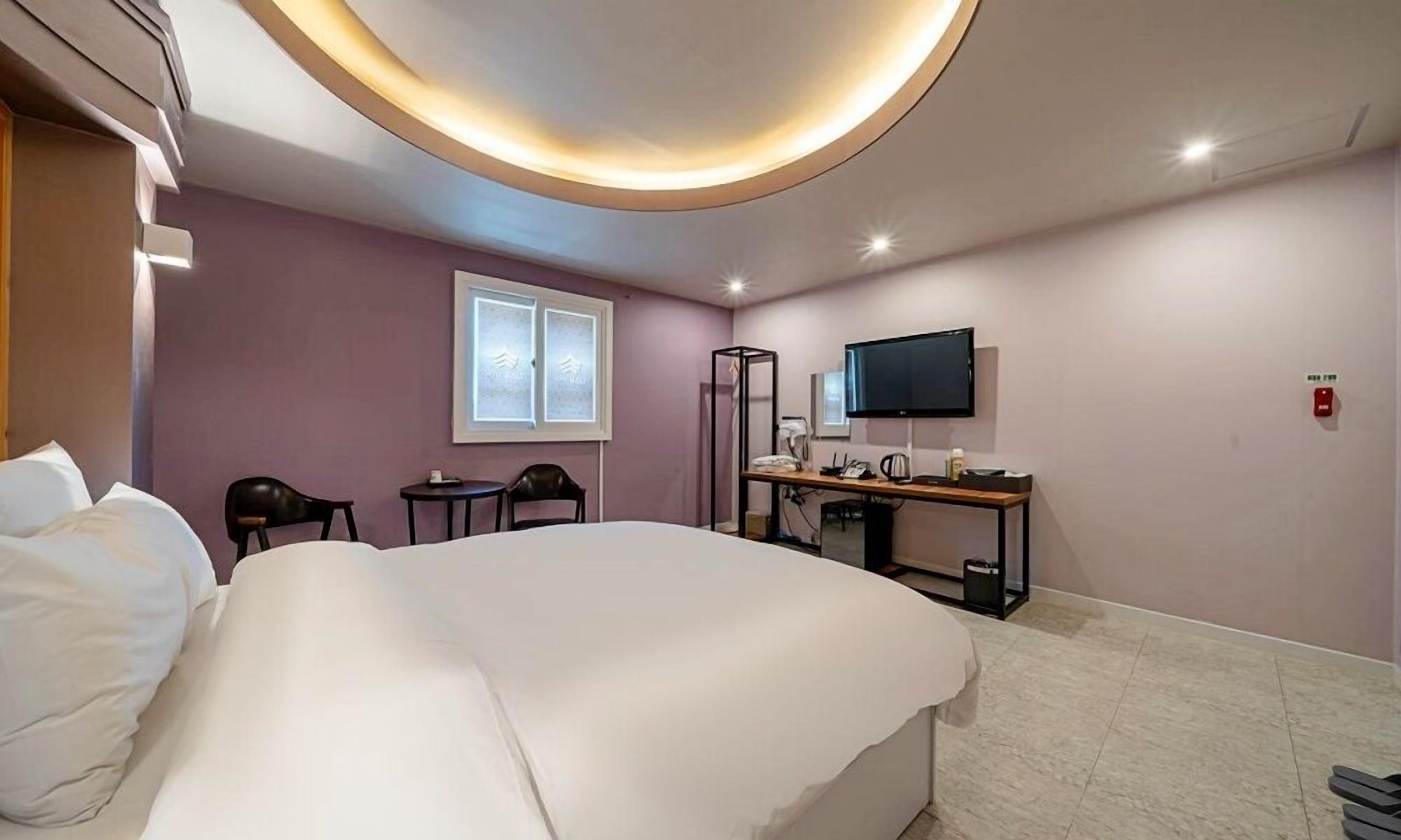 Ein Hotelzimmer mit einem großen Bett, einem Schreibtisch mit Flachbildfernseher, einem kleinen Tisch und zwei Stühlen.
